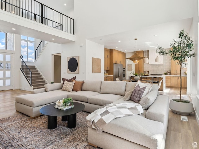 living area featuring light wood finished floors, a high ceiling, stairs, and recessed lighting