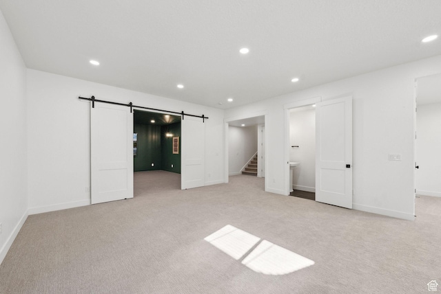 unfurnished bedroom featuring a barn door, light carpet, recessed lighting, and baseboards