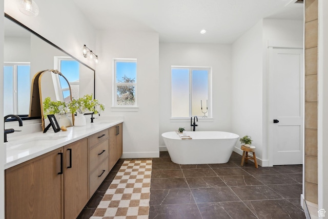 bathroom featuring a freestanding tub, baseboards, double vanity, and recessed lighting