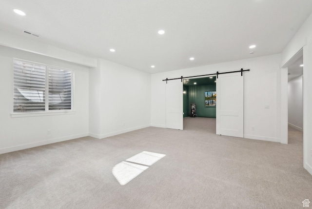 unfurnished bedroom featuring a barn door, recessed lighting, light carpet, and baseboards