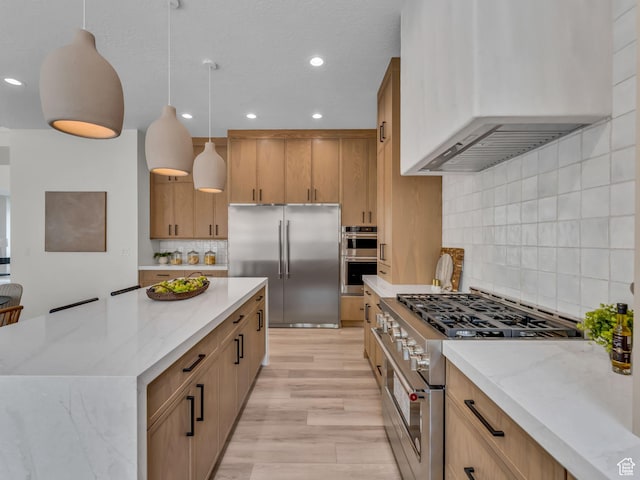 kitchen with high quality appliances, wall chimney exhaust hood, light stone countertops, tasteful backsplash, and recessed lighting