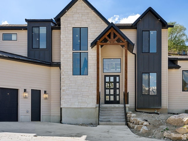 contemporary house featuring board and batten siding, stone siding, entry steps, and an attached garage