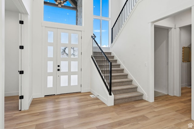 entrance foyer featuring stairway, light wood-type flooring, a high ceiling, and baseboards