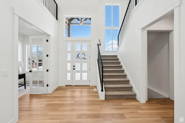 foyer featuring light wood-type flooring, stairs, healthy amount of natural light, a high ceiling, and baseboards