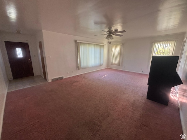 unfurnished living room with light colored carpet, plenty of natural light, a ceiling fan, and baseboards