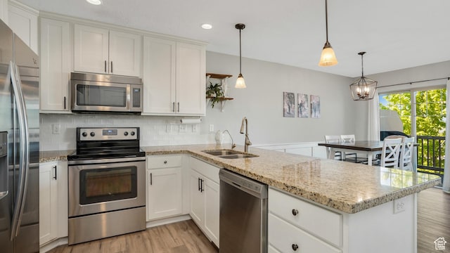 kitchen featuring appliances with stainless steel finishes, a sink, a peninsula, light wood-style floors, and decorative backsplash