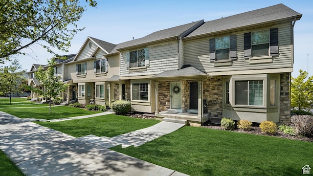 view of property featuring stone siding, a front yard, and roof with shingles
