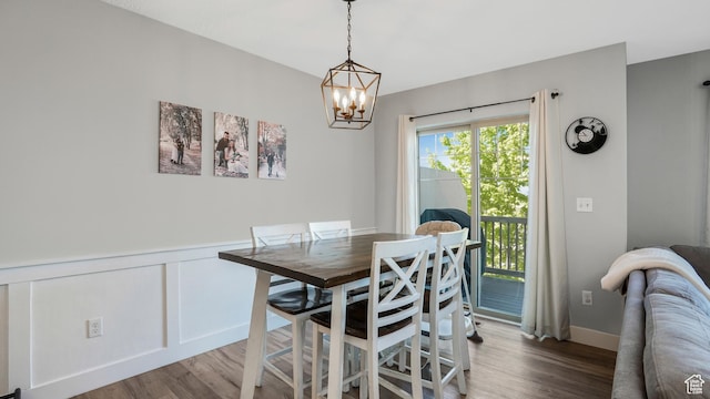dining space featuring wood finished floors, a chandelier, a wainscoted wall, and a decorative wall