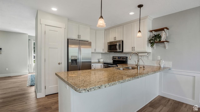 kitchen with appliances with stainless steel finishes, a sink, a peninsula, light stone counters, and dark wood finished floors
