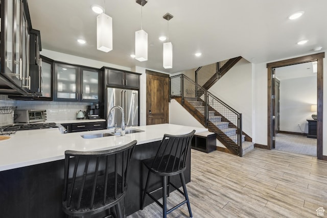 kitchen with a sink, high quality fridge, light countertops, pendant lighting, and glass insert cabinets