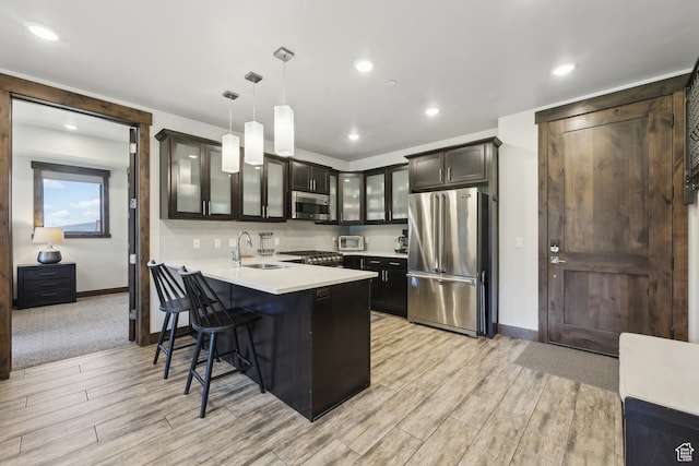 kitchen with appliances with stainless steel finishes, a sink, glass insert cabinets, baseboards, and a peninsula