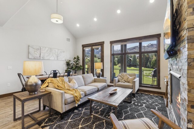 living area featuring recessed lighting, baseboards, wood finished floors, high vaulted ceiling, and a stone fireplace
