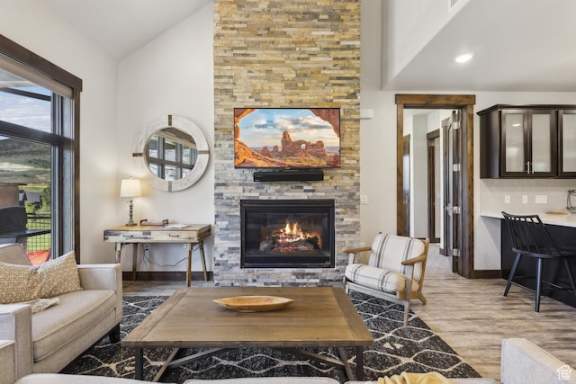 living area with a fireplace, wood finished floors, baseboards, and high vaulted ceiling