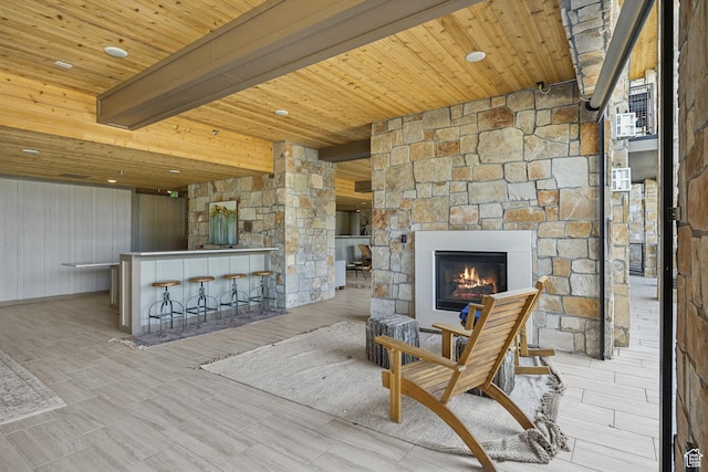 sitting room featuring a bar, wooden ceiling, a stone fireplace, and beam ceiling