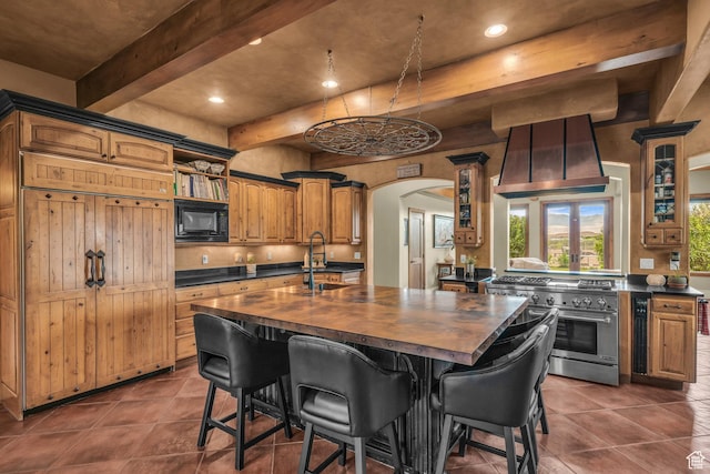 kitchen with high end stove, black microwave, a sink, butcher block countertops, and beamed ceiling