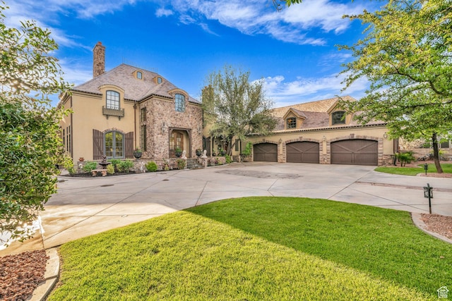 french country home featuring stone siding, driveway, a front yard, a chimney, and stucco siding