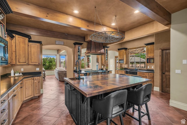 kitchen featuring a sink, wooden counters, arched walkways, premium range hood, and beam ceiling