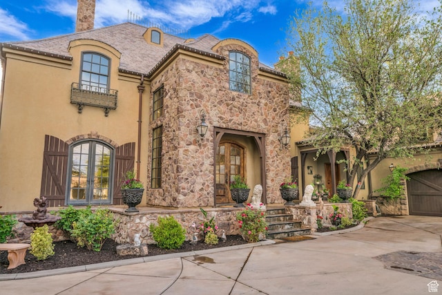 view of front of property with a chimney, driveway, stucco siding, stone siding, and french doors