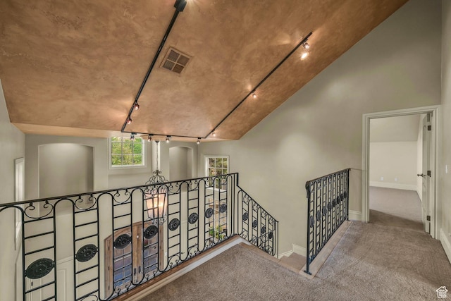 hall featuring rail lighting, an upstairs landing, carpet floors, baseboards, and arched walkways