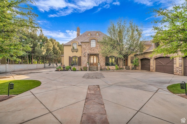 french provincial home featuring a chimney, fence, concrete driveway, stone siding, and stucco siding