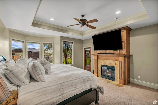 bedroom featuring a tray ceiling, ornamental molding, light colored carpet, a tile fireplace, and baseboards