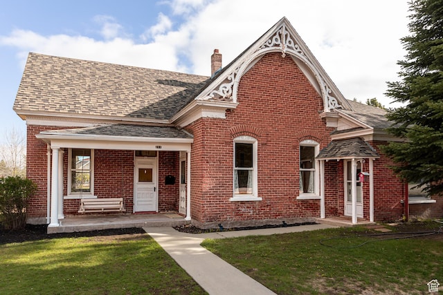 view of front of house with brick siding, a chimney, a front yard, and a shingled roof