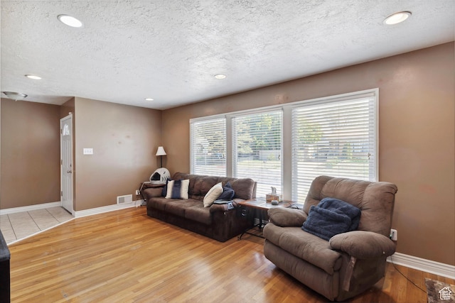 living room featuring a textured ceiling, light wood finished floors, baseboards, and recessed lighting
