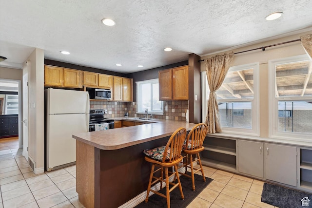 kitchen with stainless steel appliances, light tile patterned floors, a peninsula, decorative backsplash, and a sink
