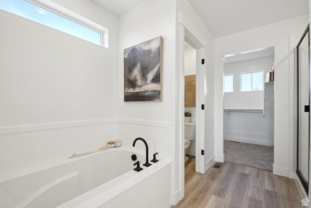 full bathroom featuring healthy amount of natural light, a bath, toilet, and wood finished floors