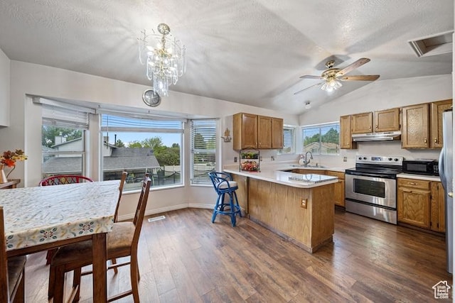 kitchen with stainless steel appliances, a peninsula, a textured ceiling, brown cabinetry, and under cabinet range hood