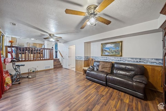 living area featuring ceiling fan, a textured ceiling, wood finished floors, a wainscoted wall, and stairs