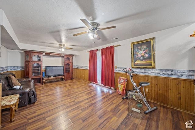 living room with wainscoting, wood walls, wood finished floors, a ceiling fan, and a textured ceiling