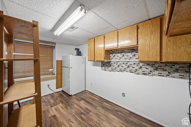 kitchen with freestanding refrigerator, a drop ceiling, tasteful backsplash, dark wood finished floors, and baseboards