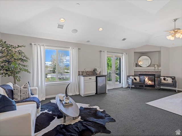 living area with dark colored carpet, a glass covered fireplace, lofted ceiling, baseboards, and a ceiling fan