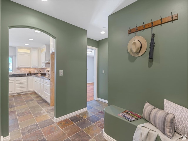 corridor with stone tile flooring, baseboards, recessed lighting, and arched walkways