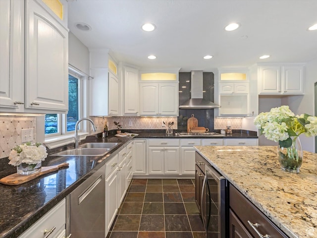 kitchen featuring wall chimney exhaust hood, a sink, stainless steel dishwasher, beverage cooler, and white cabinets