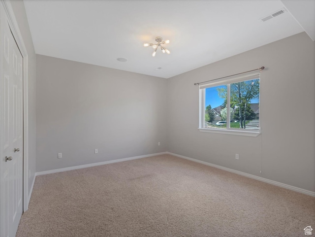 spare room featuring a chandelier, light carpet, and baseboards