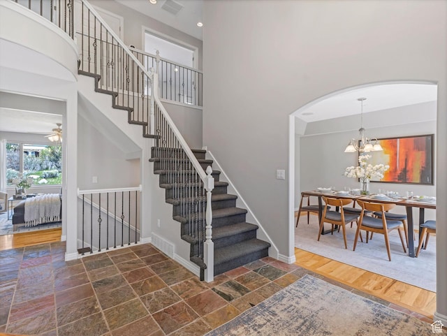 stairway with stone tile flooring, arched walkways, baseboards, a chandelier, and a high ceiling