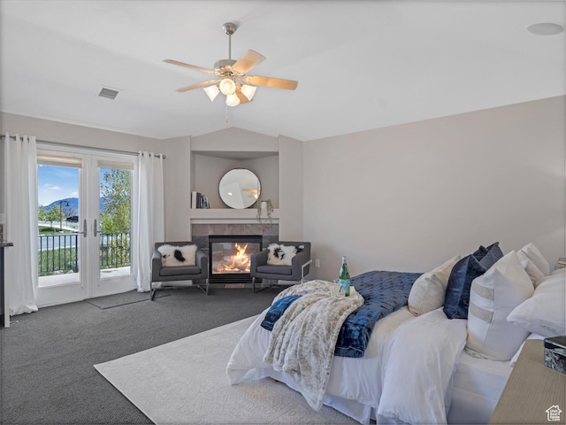bedroom featuring access to outside, lofted ceiling, carpet flooring, a tiled fireplace, and a ceiling fan