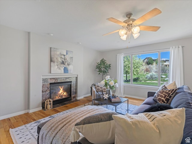 living area featuring a tile fireplace, light wood-type flooring, baseboards, and a ceiling fan
