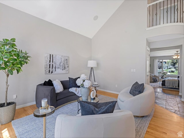 living area featuring baseboards, wood finished floors, high vaulted ceiling, and a ceiling fan