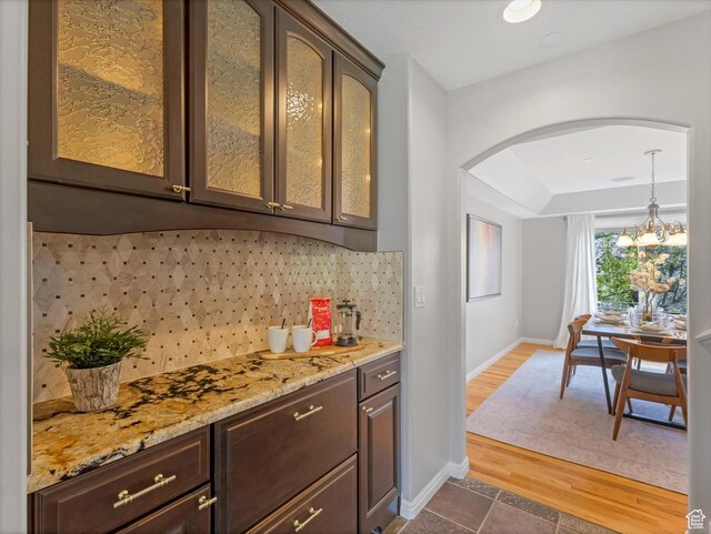 indoor dry bar with arched walkways, decorative backsplash, baseboards, decorative light fixtures, and dark wood-type flooring