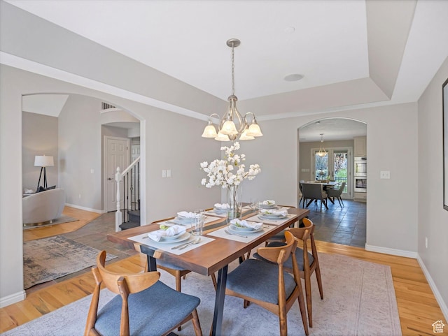 dining space featuring arched walkways, a chandelier, stairs, and light wood finished floors