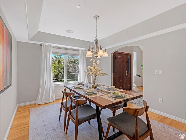 dining room with arched walkways, light wood-style flooring, baseboards, and a chandelier