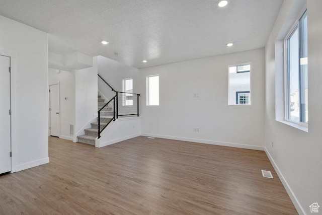 unfurnished living room with light wood-style floors, stairway, baseboards, recessed lighting, and a textured ceiling