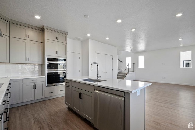 kitchen with stainless steel appliances, a sink, gray cabinetry, wood finished floors, and tasteful backsplash