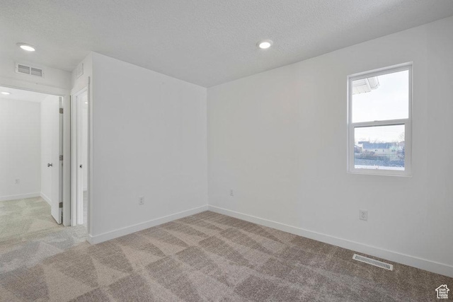 spare room with light colored carpet, a textured ceiling, baseboards, and recessed lighting