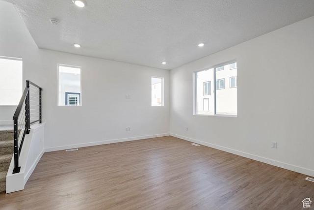 spare room featuring stairs, light wood-type flooring, a textured ceiling, baseboards, and recessed lighting