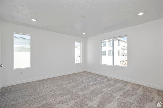 spare room featuring healthy amount of natural light, light colored carpet, baseboards, recessed lighting, and a textured ceiling