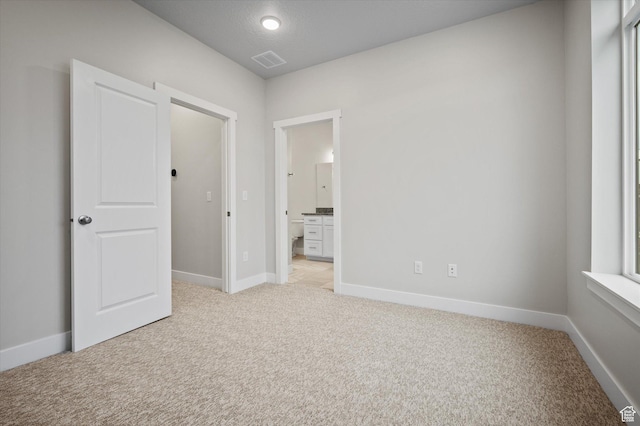 unfurnished bedroom with light colored carpet, baseboards, and ensuite bathroom